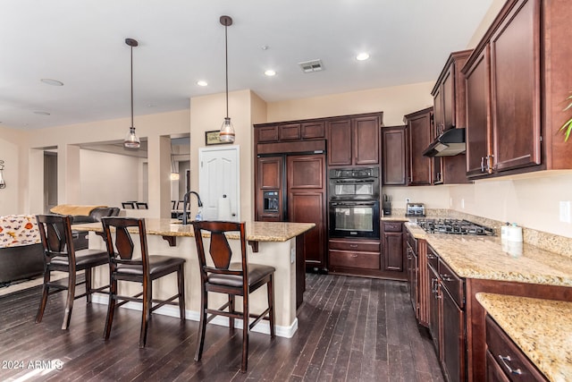 kitchen featuring paneled built in refrigerator, dark hardwood / wood-style flooring, hanging light fixtures, stainless steel gas stovetop, and a kitchen island with sink