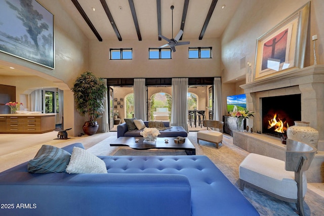 living room with ceiling fan, beam ceiling, a premium fireplace, and a high ceiling