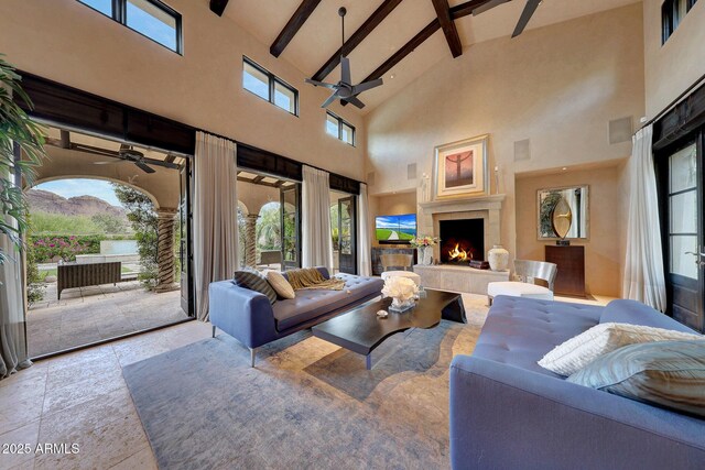 living room featuring beamed ceiling, ceiling fan, an outdoor fireplace, and a high ceiling