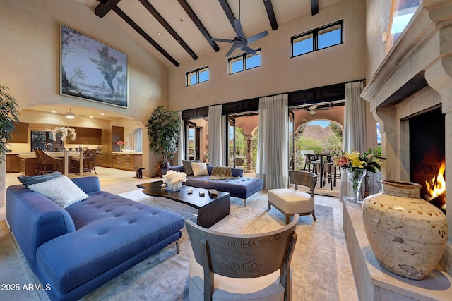 living room with beam ceiling, ceiling fan, a fireplace, and a high ceiling