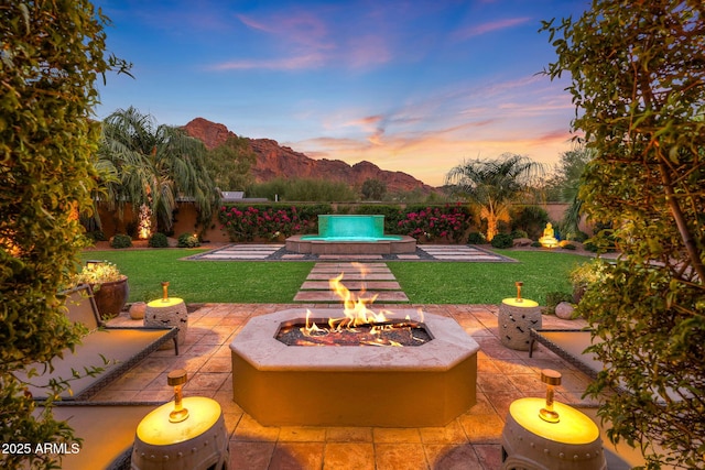 patio terrace at dusk with a mountain view, a yard, and an outdoor fire pit