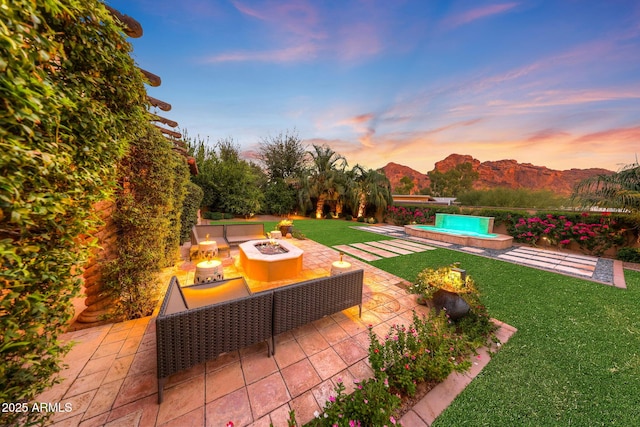 patio terrace at dusk with a fire pit, a mountain view, and a yard