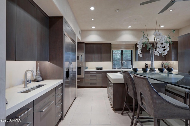 kitchen with sink, oven, a breakfast bar area, dark brown cabinets, and light tile patterned flooring