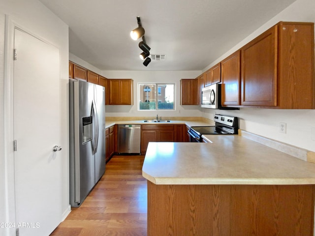 kitchen with kitchen peninsula, light wood-type flooring, stainless steel appliances, and track lighting