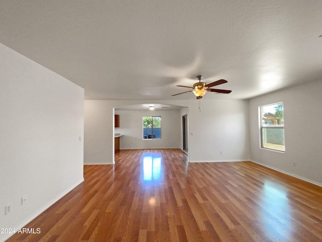 unfurnished living room featuring wood-type flooring, plenty of natural light, and ceiling fan