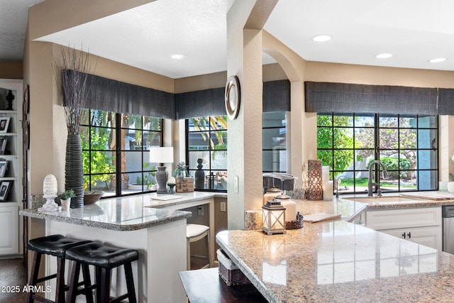 kitchen with a sink, light stone countertops, a breakfast bar, white cabinetry, and arched walkways