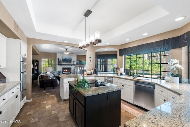 kitchen with stainless steel appliances, a tray ceiling, a ceiling fan, open floor plan, and a brick fireplace