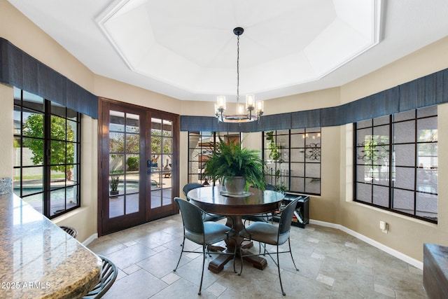 dining area featuring a tray ceiling, french doors, a chandelier, baseboards, and stone tile floors