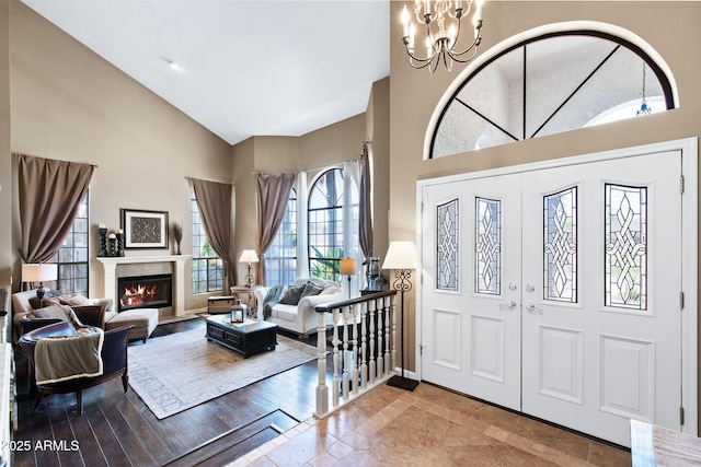 foyer entrance featuring high vaulted ceiling, a chandelier, french doors, a lit fireplace, and baseboards