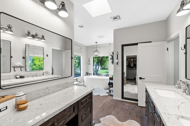 bathroom featuring a skylight, wood finished floors, a soaking tub, and two vanities
