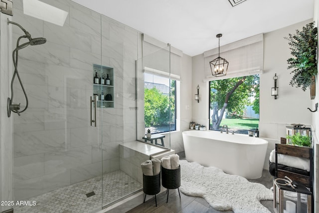 full bath featuring a shower stall, a freestanding bath, a chandelier, and tile walls