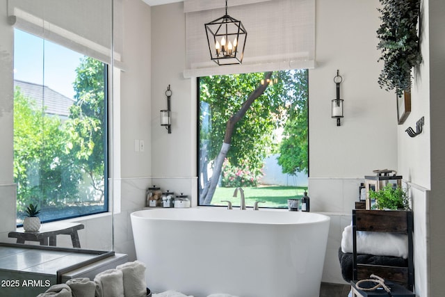 full bath featuring tile walls, a freestanding bath, and a chandelier