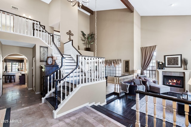 stairs featuring a towering ceiling, arched walkways, baseboards, and a fireplace