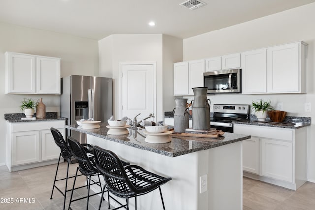 kitchen with appliances with stainless steel finishes, a center island with sink, visible vents, and white cabinets