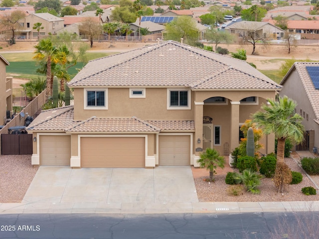 mediterranean / spanish-style home featuring stucco siding, a tile roof, a garage, and fence