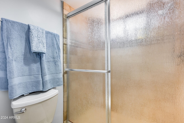 bathroom featuring toilet and a shower with shower door