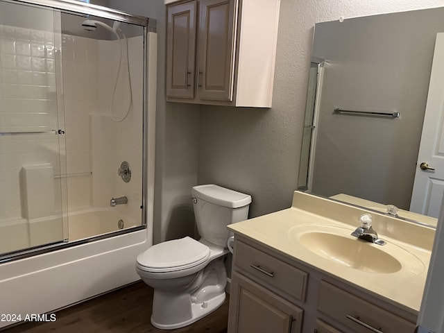 full bathroom with shower / bath combination with glass door, hardwood / wood-style floors, vanity, and toilet