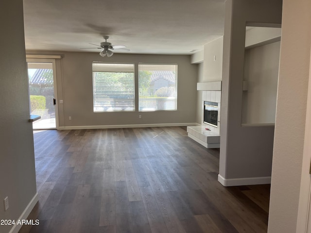 unfurnished living room with a tile fireplace, ceiling fan, and dark wood-type flooring