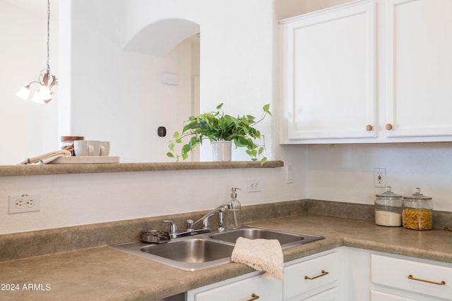 kitchen with hanging light fixtures, white cabinetry, sink, and a notable chandelier