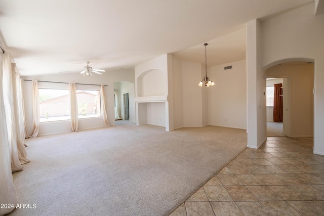 unfurnished living room featuring ceiling fan with notable chandelier, vaulted ceiling, and light colored carpet