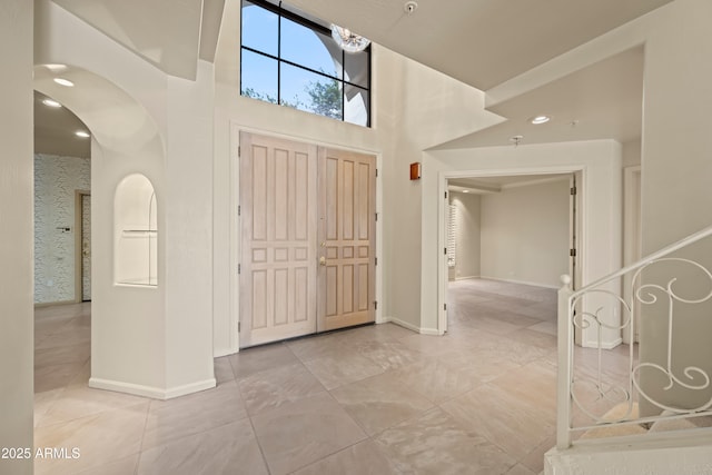 entryway with arched walkways, baseboards, and a high ceiling