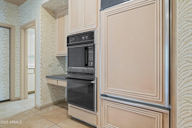 kitchen featuring light tile patterned floors, dobule oven black, cream cabinets, baseboards, and wallpapered walls