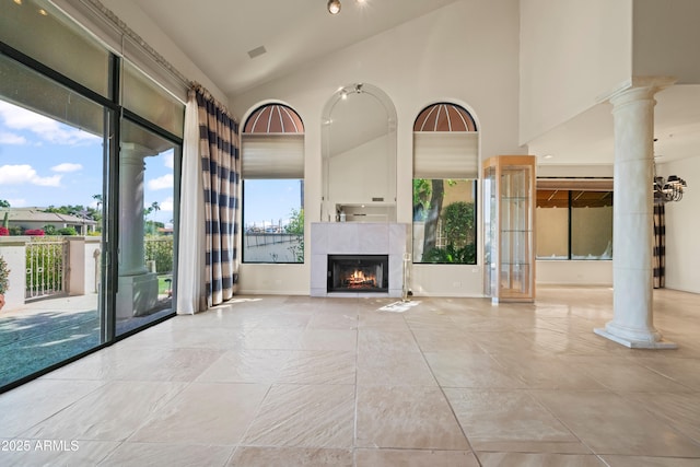 unfurnished living room with baseboards, high vaulted ceiling, a tiled fireplace, and ornate columns