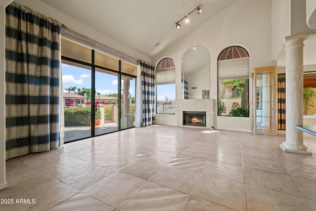 unfurnished living room featuring high vaulted ceiling, a tile fireplace, rail lighting, and ornate columns