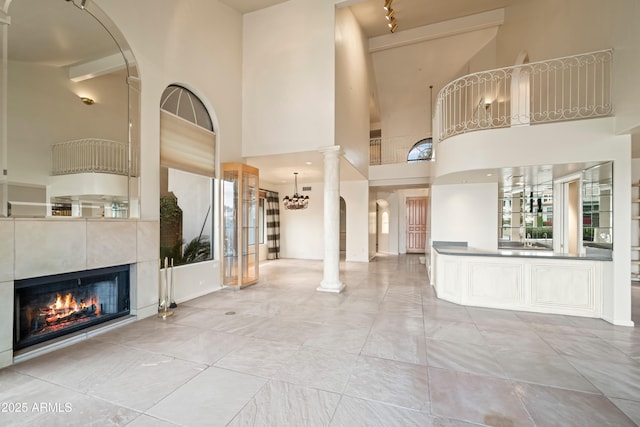 unfurnished living room with a high ceiling, a tiled fireplace, an inviting chandelier, and ornate columns