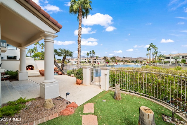 view of patio / terrace featuring a residential view, a water view, fence, and a lit fireplace