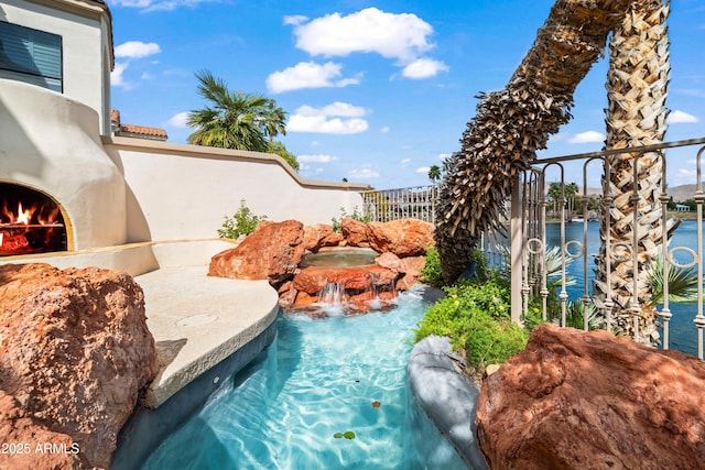 view of swimming pool featuring a lit fireplace and fence