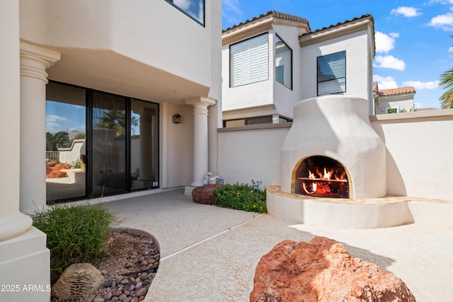 view of exterior entry featuring a warm lit fireplace, a tile roof, and stucco siding