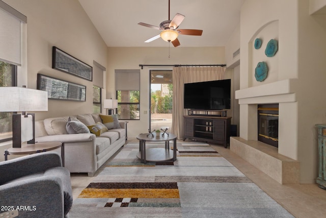 living room with a towering ceiling, visible vents, a ceiling fan, and a glass covered fireplace