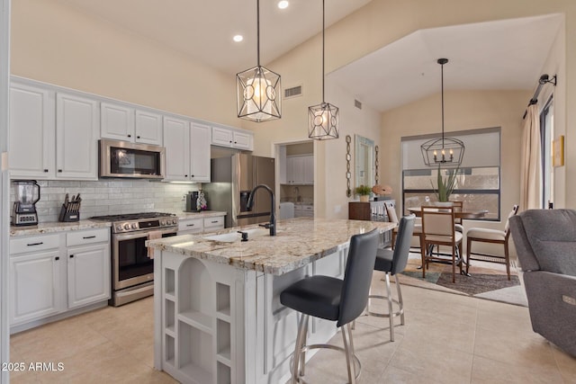 kitchen featuring stainless steel appliances, tasteful backsplash, white cabinets, a sink, and an island with sink