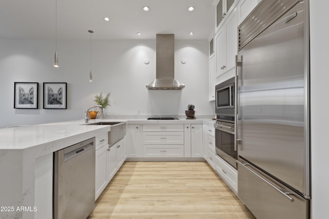 kitchen with built in appliances, hanging light fixtures, white cabinetry, and island exhaust hood