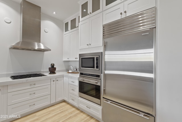 kitchen with white cabinetry, island exhaust hood, built in appliances, and light hardwood / wood-style floors