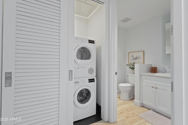 laundry area with stacked washer / drying machine and light wood-type flooring