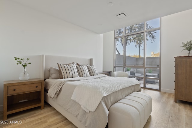 bedroom with access to exterior, a wall of windows, and light hardwood / wood-style floors