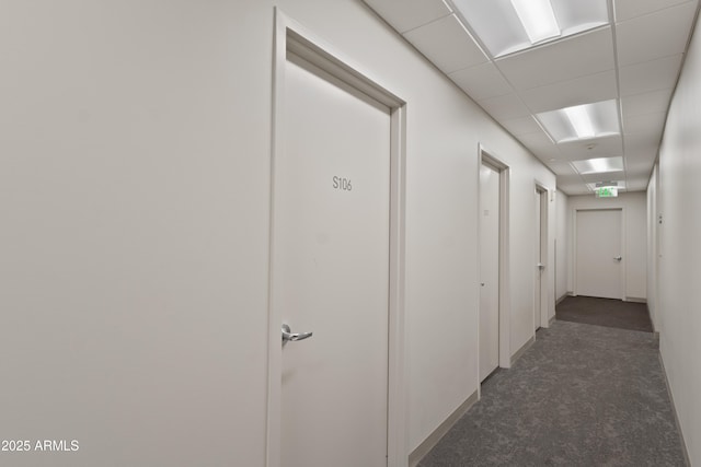 corridor featuring dark carpet and a paneled ceiling