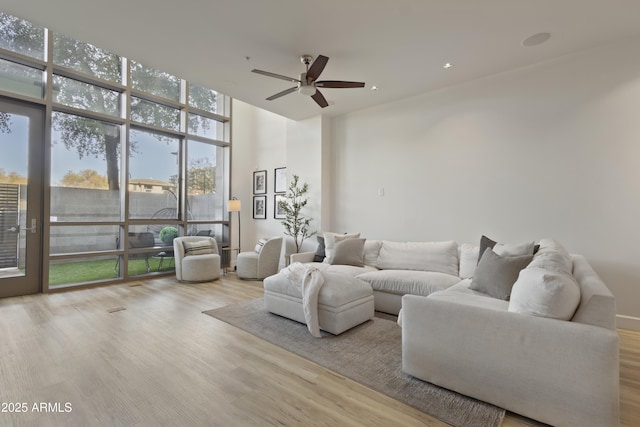 living room featuring ceiling fan, a wall of windows, and light hardwood / wood-style flooring