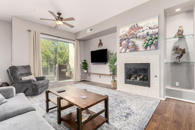 living room featuring a tiled fireplace, hardwood / wood-style flooring, and ceiling fan