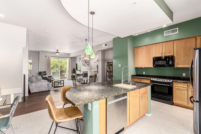 kitchen featuring a breakfast bar, sink, hanging light fixtures, an island with sink, and black appliances