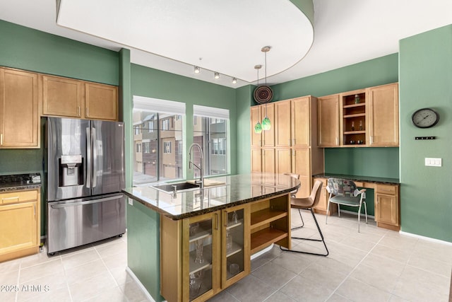 kitchen featuring sink, built in desk, stainless steel fridge with ice dispenser, a center island with sink, and dark stone countertops