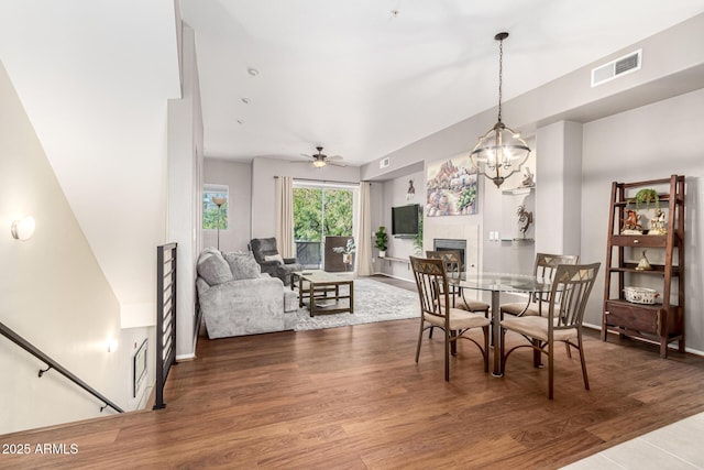 dining room with a tile fireplace, wood-type flooring, and ceiling fan with notable chandelier