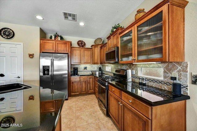 kitchen with glass insert cabinets, visible vents, appliances with stainless steel finishes, brown cabinets, and decorative backsplash