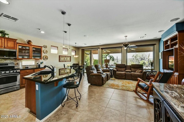 kitchen featuring brown cabinetry, visible vents, appliances with stainless steel finishes, a sink, and dark countertops