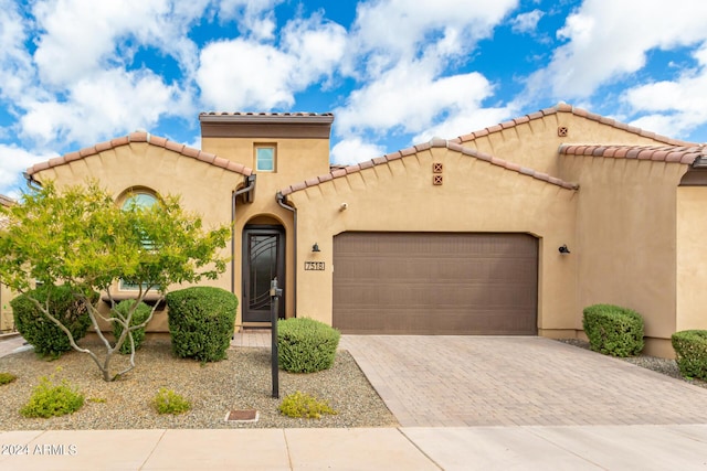 mediterranean / spanish house with decorative driveway, an attached garage, a tile roof, and stucco siding