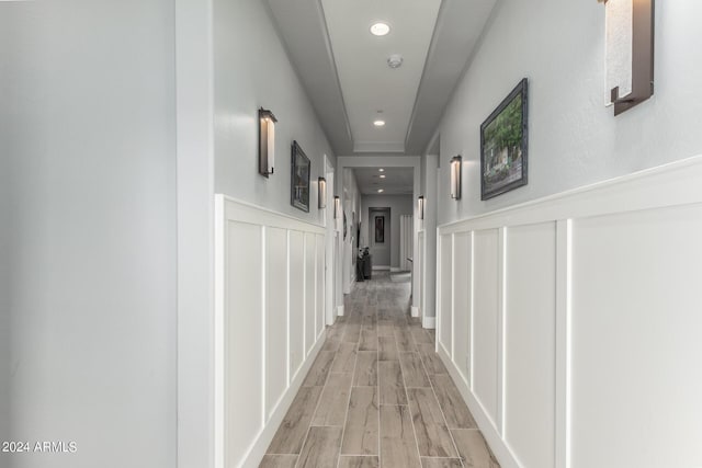 hall with light wood finished floors, a decorative wall, a wainscoted wall, and recessed lighting