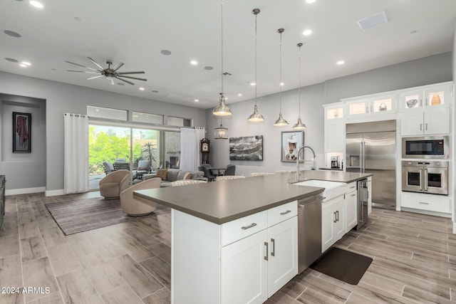 kitchen with wood finish floors, dark countertops, open floor plan, a sink, and built in appliances