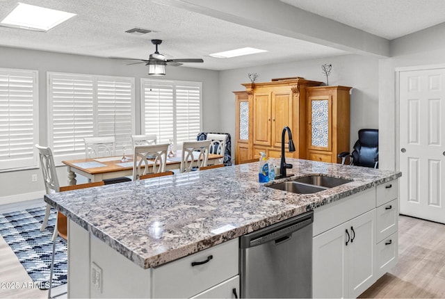kitchen with a sink, dishwasher, an island with sink, a ceiling fan, and light wood-type flooring